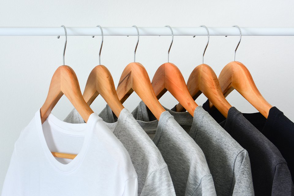 A collection of black, gray and white t-shirts hanging on wooden clothes hanger in a closet.